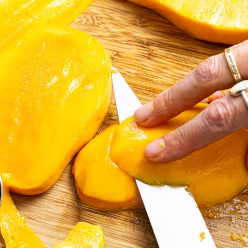 hand slicing mango half lenghtwise.