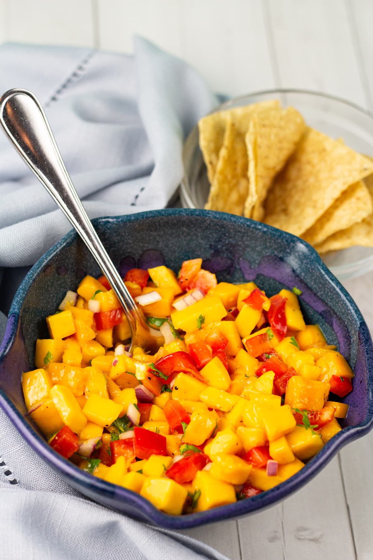 mango salsa in bowl with spoon and tortilla chips.